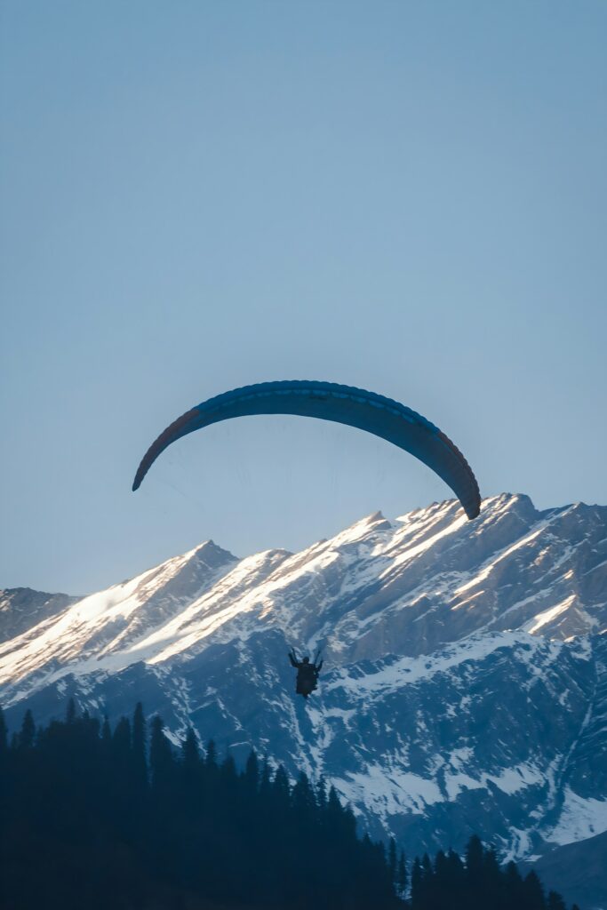 Tourists enjoying paragliding adventure over scenic valleys in Manali, Himachal Pradesh