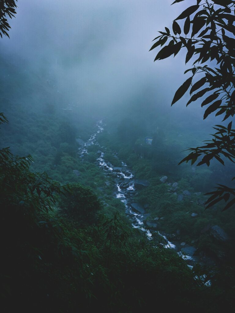 Aerial view of a scenic waterfall water channel flowing through lush green mountains in McLeod Ganj, Himachal Pradesh