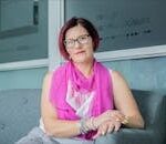 Portrait of a confident woman sitting indoors wearing glasses and pink scarf.
